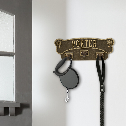 Dog Bone Leash Hooks for Wall in Antique Brass Hanging on White Wall Next to Grey Window Frame Holding a Key Chain and Leash